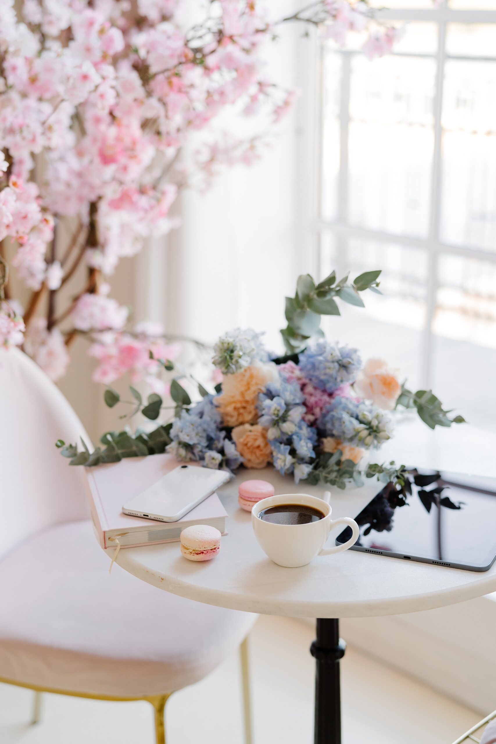 A room with blue, yellow, and pink flowers, with a small table that has a coffee, tablet, phone, and book.